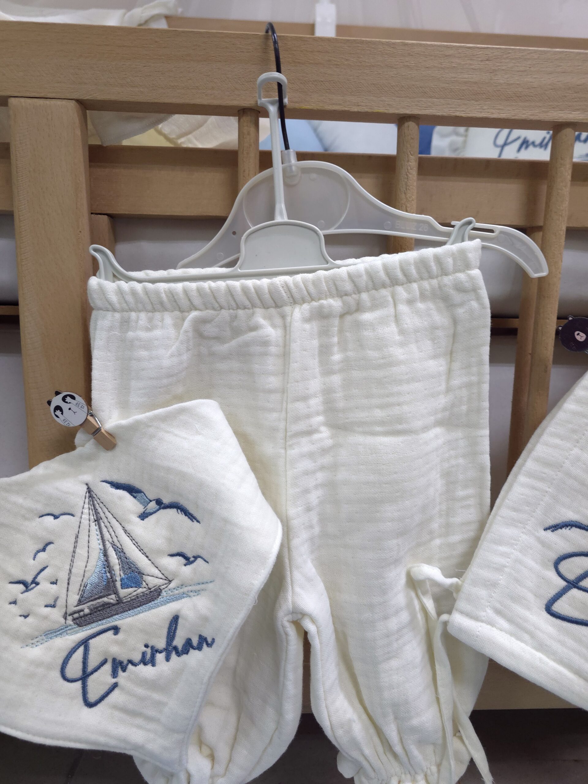 müslin-hastane-çıkışı-T13-(6) 4 katlı %100 pamuk müslin hastane çıkışı seti (0–3 ay); isimli nakışlı tulum, şapka, alt üst takım, eldiven, önlük, battaniye, puset örtüsü ve kırlent ile eksiksiz bir yenidoğan seti sunar.